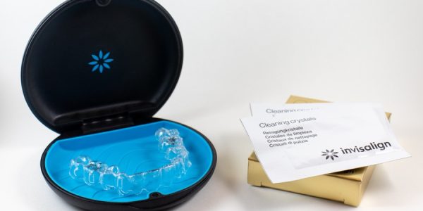 Invisalign braces or invisible transparent aligner on white background. invisalign blue package with a box and cleaning crystals.